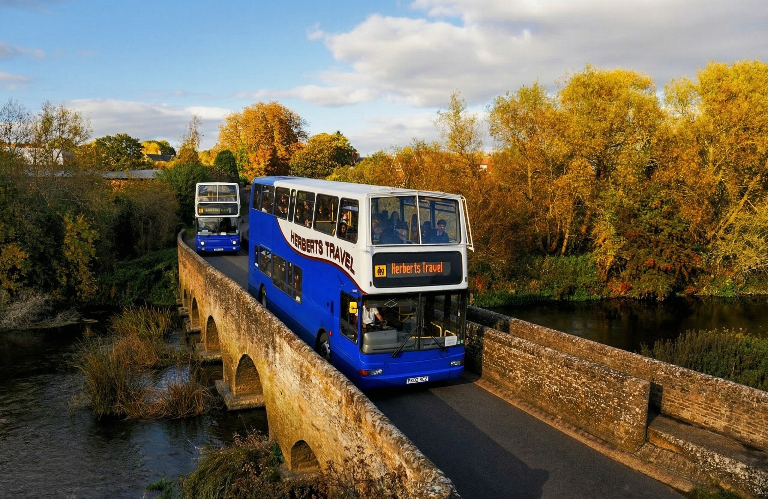 Herberts Travel coaches crossing stone bridge at golden hour
